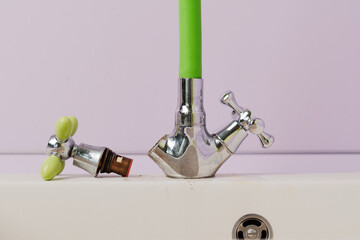Old faucet handle with valve cartridge lies beside shiny tap with green hose, illustrating...