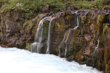 Obraz premium multiple thin waterfalls falling over a bare red rock into a rapid flowing mountain stream