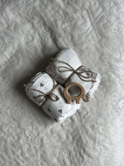 Two twisted muslin diapers and an elephant teether are lying on a milky-colored blanket. Children's...