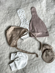 Beige and white hats with stars, a bonnet, and scratches lie on the light blanket of the bed in the...