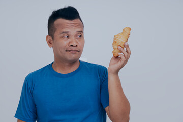 Bored Asian man having breakfast with croissant.