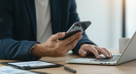 Business professional working remotely with smartphone and laptop in modern office setting