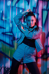 Stylish woman posing confidently in front of vibrant urban graffiti at night
