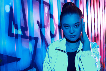 Stylish woman poses confidently against vibrant urban graffiti backdrop during night