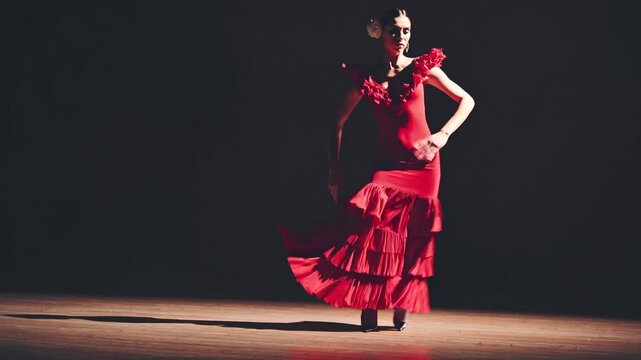 Passionate female flamenco dancer performing with intense emotion, wearing vibrant red dress and moving gracefully on darkened theater stage