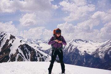 A female tourist fastens the belt of a tourist backpack against the background of snowy mountains.