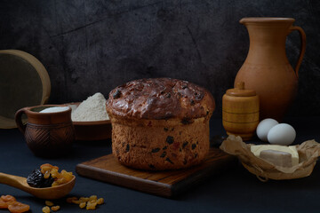 Homemade easter cake rises in a rustic kitchen, surrounded by utensils and  essential baking ingredients like flour, sugar, eggs, butter, dried fruits, yeast