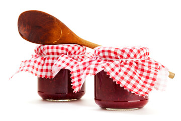 Two jars of homemade jam and wooden cooking spoon isolated on white background