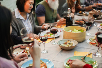 Family and friends eating and driking red wine at bbq meal outdoor - Different age of people having fun at barbecue dinner - Summer lifestyle and fun concept - Main focus on bottom wine glass