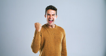 Man, celebration and fist pump in studio portrait with shout, success and goals by background....