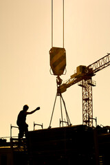 silhouette of construction worker conducting crane lifting load
