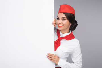 A smiling flight attendant dressed professionally in uniform holding a blank white board in a...