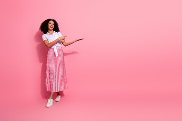 Young woman in stylish pink outfit pointing sideways on vibrant pink background, highlighting...
