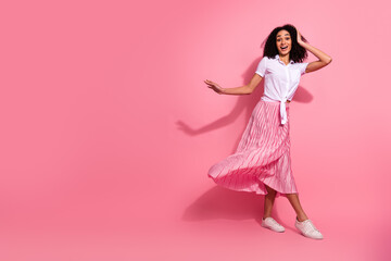 Joyful young woman in stylish summer attire twirling playfully against a vibrant pink background,...