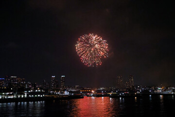 Fireworks explode in the sky over Yokohama Port, with the city skyline in the background
