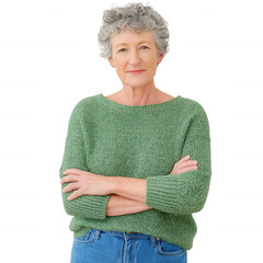 Confident older woman with curly hair standing with arms crossed, smiling softly, wearing a cozy green sweater and blue jeans against white background.