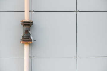 Urban industrial structure featuring a weathered pipe and a metallic joint against a minimalist gray wall during midday