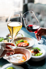 Two people clinking glasses of white and red wine over a table with various dishes, creating a celebratory and elegant dining atmosphere