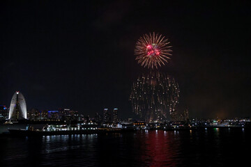 Fireworks explode in the sky over Yokohama Port, with the city skyline in the background