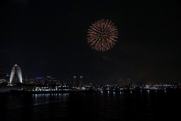 Fireworks explode in the sky over Yokohama Port, with the city skyline in the background