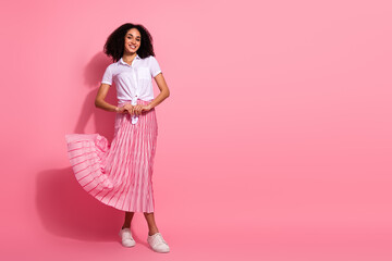Young woman in stylish pleated pink skirt and white shirt posing on pink background, promoting fashion and lifestyle