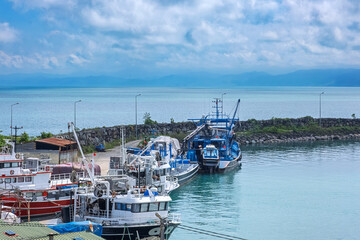 Fototapeta premium Fishing boats docked in coastal harbor. A cluster of fishing boats docked at coastal harbor under cloudy sky. This peaceful maritime view captures the essence of coastal life and the fishing industry.