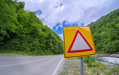 Warning sign by a winding road. A close-up view of a triangular warning sign alongside a winding road. The image conveys a sense of caution and adventure. Use for idea related to travel and safety.