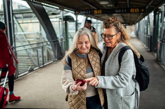 Two senior women looking at smartphone for directions at a train station - Powered by Adobe
