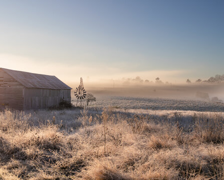 A country scene on a misty morning with a broken windmill and an old country barn