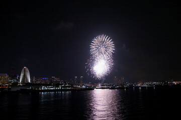 Fireworks explode in the sky over Yokohama Port, with the city skyline in the background