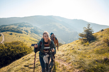 Couple hiking uphill on scenic mountain trail with backpacks and trekking poles