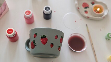 Process of painting a grey ceramic cup with red strawberries using acrylic paints.