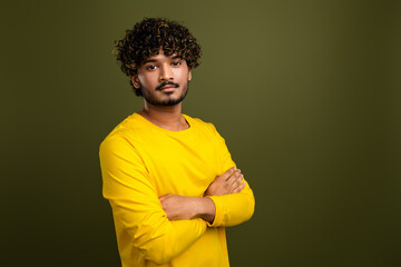 Portrait of a confident young man in a yellow shirt with curly hair posing against a green...