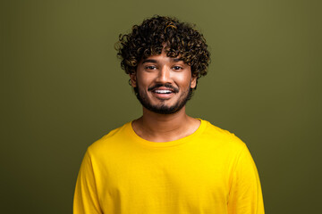Obraz premium Smiling young man with curly hair wearing a yellow shirt standing against a neutral khaki background portrait shot