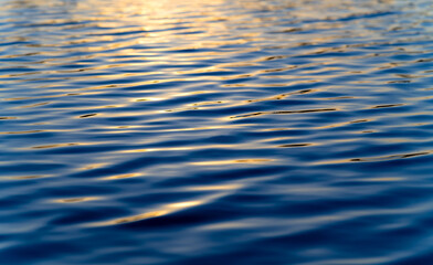 Water surface with calm waves and reflection of blue evening sky and warm sunset twilight at a big lake in Sauerland Germany. Liquid background with bright blue and orange colors and gradients.