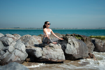 sporty woman sitting on rocks by the sea meditating