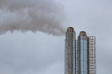Industrial factory smokestacks emitting thick gray smoke into cloudy sky, air pollution concept.
