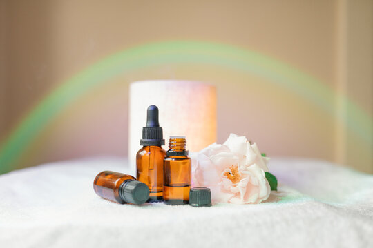 Collection of amber essential oil bottles with fresh rose, diffuser and rainbow light effect