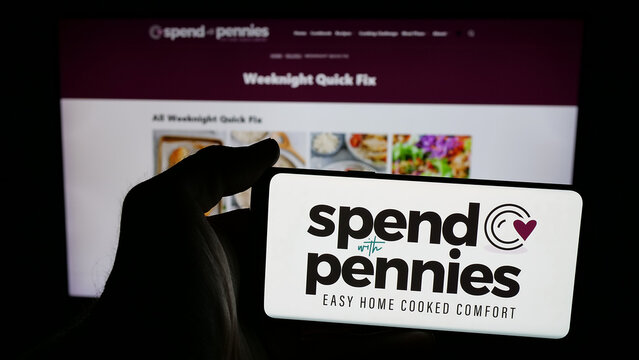 Stuttgart, Germany - 05-26-2025: Person holding mobile phone with logo of company Spend With Pennies (SWP Media Ltd.) on screen in front of web page. Focus on phone display.