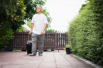 Elderly Gentleman with Suitcase Walking in a Residential Area, Senior Asian Man Traveling with Luggage Outdoors, Retired Man on Vacation or Business Trip Ready to Go