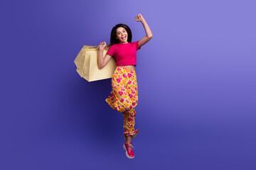 Young woman with vibrant style celebrating and carrying shopping bags against colorful backdrop,...