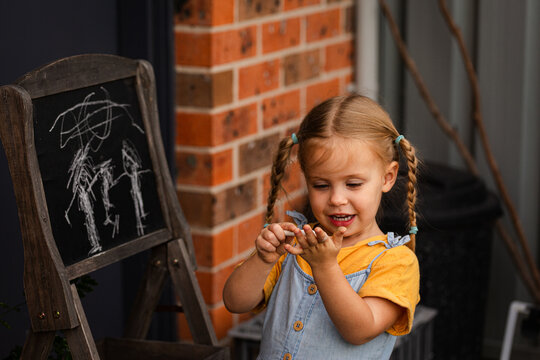 Little girl standing outside in backyard drawing her family on chalkboard