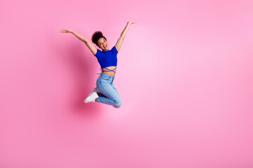 Young woman jumps joyfully on pink background, wearing casual fashion, expressing happiness and fun...