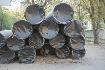 Piled black pipes ready for construction near a riverbank in springtime sunshine