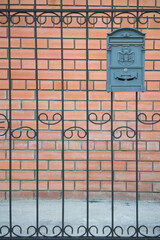 Decorative wrought iron fence with intricate patterns surrounds a brick wall, featuring a vintage mailbox attached, creating a charming and inviting entrance to a property