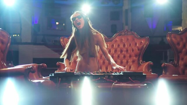 Sexy woman mixing music at the club. Glamorous female DJ. Funny dj enjoying nightlife. Sexy clubbing girl with a headset. Pretty woman dancing to electronic music. Luxury nightclub scene with a DJ.