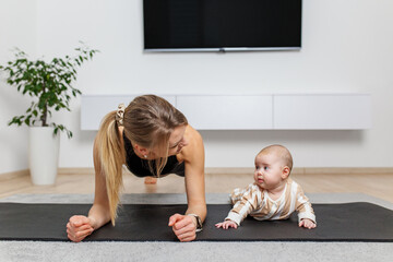 Mother planking next to baby on yoga mat.
