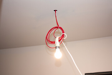 Red and white wires hanging from the ceiling with a glowing light bulb and no fixture