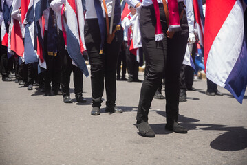 Participants in a Costa Rica Independence Day parade carry flags while marching in coordinated formation on a sunny day. 