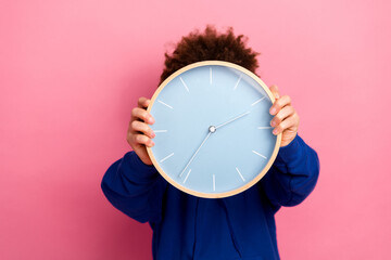 Young boy holding a modern clock in front of his face against a vibrant pink background, expressing time management and playful vibes